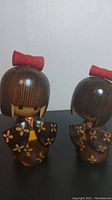 Two wooden dolls side by side with floral painted kimono and red bows on hair.