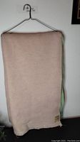 Full view of the folded pink wool blanket with fringes, hanging on a wire hanger.