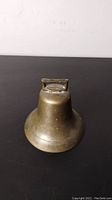 Side view of antique brass cowbell showing shape and patina with paint speckles