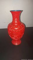 Front view of red cinnabar vase showing detailed carved village scene and shape of vase.