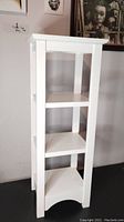 Front view of the white wooden side table display shelf showing three shelves and four supporting legs.