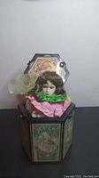 Front view with open lid showing Sleeping Beauty doll with brown hair and colorful fabric collar inside hexagonal box.