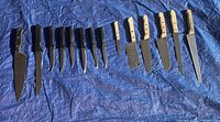 Photo of 14 knives laid out on a blue tarp, showing black and wooden handles and a variety of blade types for cutting and slicing.
