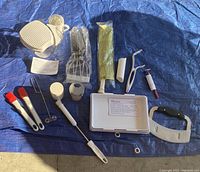 Photo shows 15 Pampered Chef miscellaneous kitchen tools arranged on a blue tarp including colander, pastry cutter, bunch of brushes, peelers, and other gadgets.