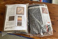 Two sealed quilting kits showing fabric bundles and printed pattern sheets on wood table.