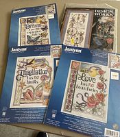 Four cross stitch kits displayed showing cover artwork with inspirational quotes and colorful designs by Janlynn and Design Works.