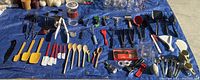 Top-down photo of 64 kitchen utensils laid out on blue tarp including spatulas, spoons, peelers, whisks, ladles, measuring implements, and other tools.