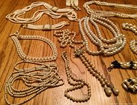 Assorted faux pearl necklaces and bracelets laid flat on wood surface; various strand styles visible