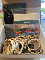 Photo showing a craft starter kit with a Chakra Mandalas booklet, 14ct Aida fabric, multiple colored embroidery floss skeins, and eight wooden embroidery hoops.