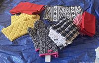 Photo of assorted kitchen textiles including yellow hot gloves and pot holder, black and white paisley hot gloves, black and white kitchen towels, red and black and white placemats, and red and mauve cloth napkins.
