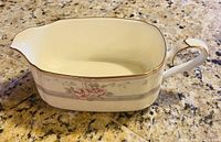 Gravy boat with handle and spout in Noritake bone china with floral pattern and gold trim.