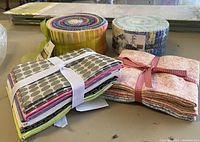 Photo showing two jelly rolls and two bundles of fabric squares in various colors and patterns arranged on table.