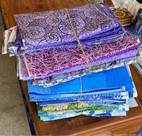 Stack of various quilting fabric cuts in shades of purple, blue, and green with swirl and abstract prints, tied with string.