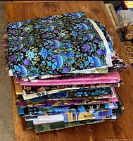Stack of folded quilting fabric showing varied floral and nature-inspired patterns in blue, purple, black, and other colors