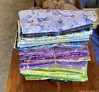 Stacked fabric bundles tied with string showing a variety of blue, black, floral, purple, green, yellow cotton quilting fabric pieces