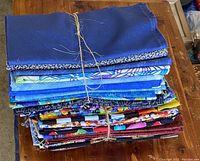 Three bundles of folded quilting fabric stacked on a wooden surface, tied with twine, showcasing different colors and patterns including blue hues, florals, and geometric prints.