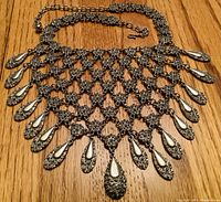 Photo of a silver-toned bib necklace with intricate chainmail-like grid and multiple oval teardrop pendants.