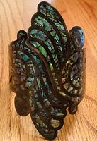 Wide cuff bracelet featuring abalone shell inlay within swirl cutout design on dark metal base.
