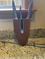 Three knives inserted into wood wall mount block with sharpening steel rod on countertop