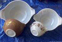 Top view of four vintage Pyrex Early Americana mixing bowls showing white glazed interiors and decorative exteriors with roosters and wheat patterns.