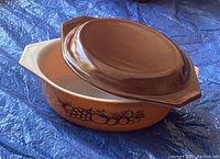 Photo of vintage Pyrex Old Orchard 1.5 quart oval casserole dish with matching brown lid, showing the fruit pattern on the side and white interior.