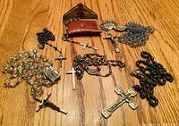 Photo of six rosaries with various bead colors and metal crucifixes, plus a red and brown pouch