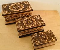 Three nesting wooden boxes with carved floral and scrollwork patterns stacked from largest to smallest