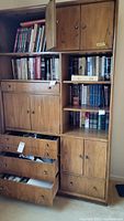 Full view of wooden shelving unit with multiple cabinets and drawers partially open, containing numerous books