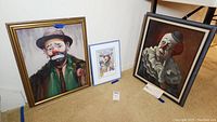 Group view of two gold-framed clown paintings and one small framed print
