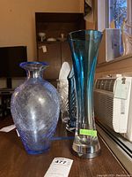 Photo showing side angle of both vases: tall blue Movado vase and shorter blue crackle glass vase.