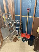 View showing the aluminum step ladder, two mobility walkers, snow shovel with red handle, brooms, dustpan, swivel sweeper and trash bin stored corner.