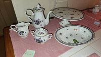 Photo of Fleetwood teapot, creamer, sugar dish, Richard Ginori cake plate and serving bowl on a pink cloth showing the full set.