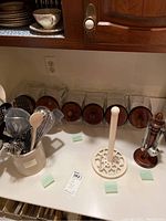 Overall kitchen counter with ceramic crock holding utensils, glass jars with wooden lids arranged behind and paper towel holder visible, showing complete set.