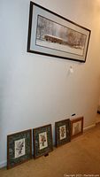 Wide shot showing one large horizontal wall art piece hanging and four smaller framed botanical prints leaning against wall below it.