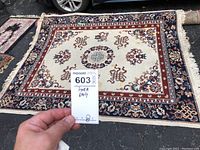 Full view of the cream colored area rug with intricate patterns and a MaxSold tag.