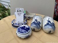 Five Blue Delft ceramic items: lidded trinket box, ashtray and three decorative shoes with blue hand-painted designs on white porcelain.