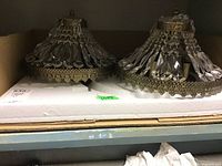 Pair of vintage brass and crystal ceiling light fixtures on a shelf with cardboard backing, light reflecting off prisms