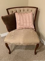Front view of beige floral patterned upholstered chair with tufted backrest and two pillows (pink and brown) on seat.