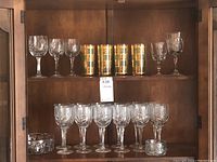 Close-up of top shelf showing 4 green vintage glasses with detailed gold trim and 5 clear crystal stemware glasses on the right side.