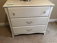 Full view of painted white dresser showing 3 drawers and decorative handles, with lamp on top not included in sale.