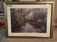 Image showing the framed landscape print hanging on a wall, depicting a wooded path with trees in fall colors.
