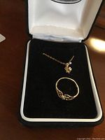 Photo of a 10K gold ring with one missing stone and a gold necklace with pendant inside a black velvet jewelry box.