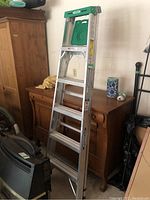 Full view of Werner aluminum A-frame ladder standing upright near cabinet and items in background