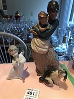 Two Lladro porcelain figurines on table: angel playing flute and mother with baby and dog