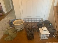 Photo showing metal lanterns of various sizes and styles, metal wall plant hangers, and a large planter with decorative metal stand.