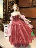 Full view of Royal Doulton lady figurine in pink dress with shawl, displayed against a brick background.