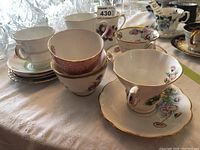 Overview of several tea cups and saucers showing different floral designs and gold trim, plus mug with Charles and Diana image