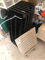 Folded black resin shelving units stacked, beige folding table leaning in front.