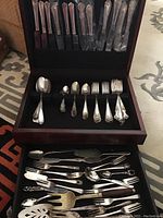 Wooden case opened showing organized silver plate flatware including knives in top slots and various spoons and forks in bottom drawer.
