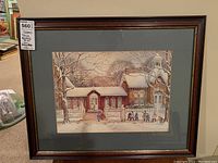Framed print of snowy brick building with children outside, hung on wall.